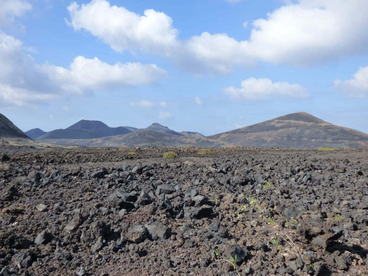Champ de lave hérissé de blocs sombres et volcans bleutés