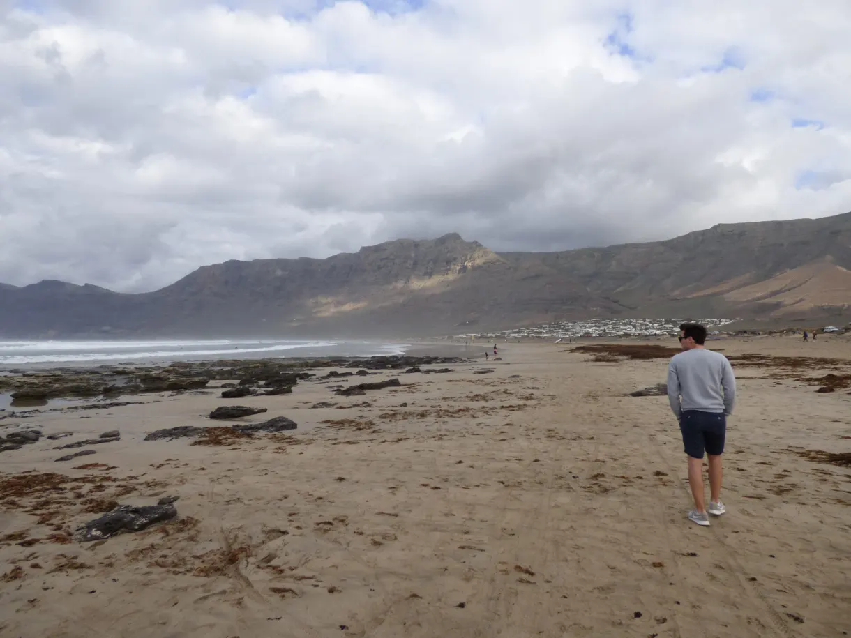 Homme marchant sur le sable face aux falaises de Famara