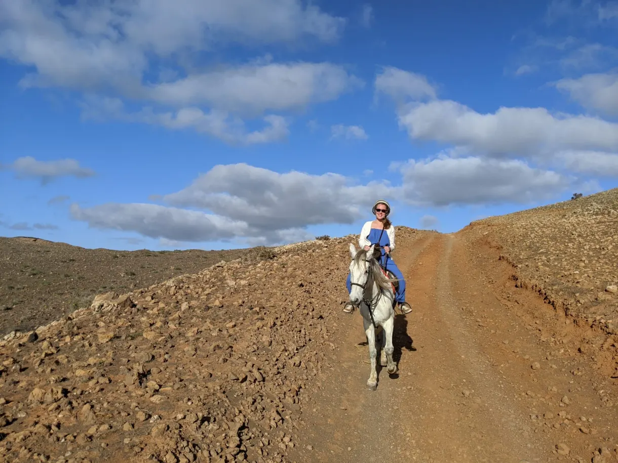 Cavalière remontant une piste ocre sous les nuages