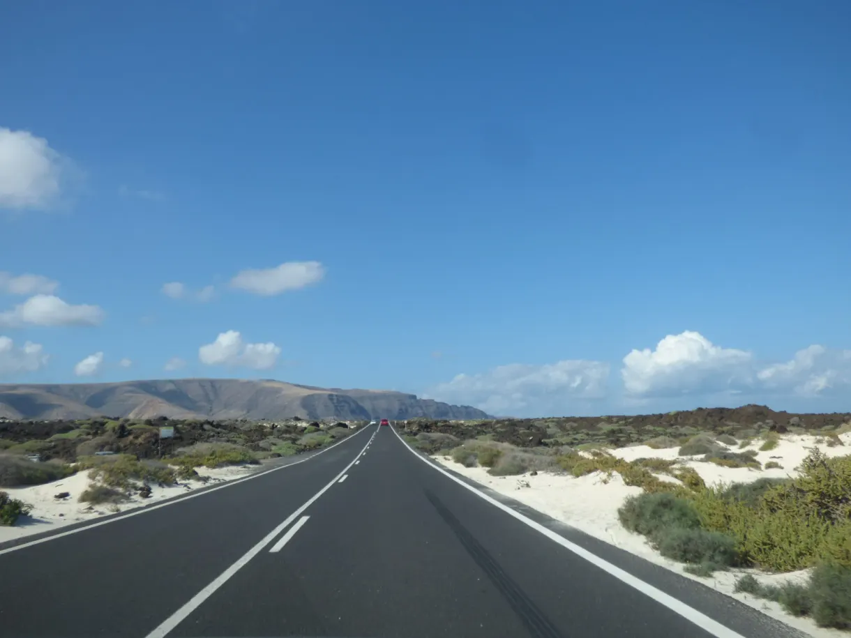 Route rectiligne filant entre sable clair et champ de lave