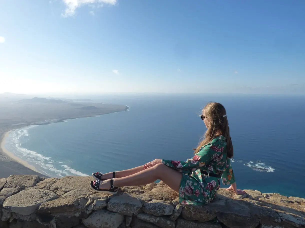 Femme assise sur le muret devant la grande baie de sable
