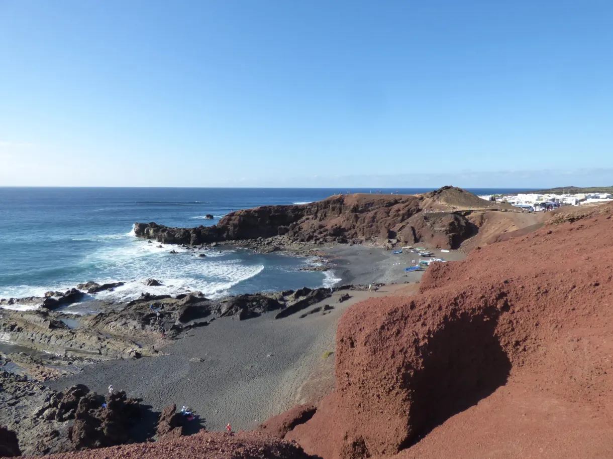Plage de galets noirs et roches rouges face à l'océan