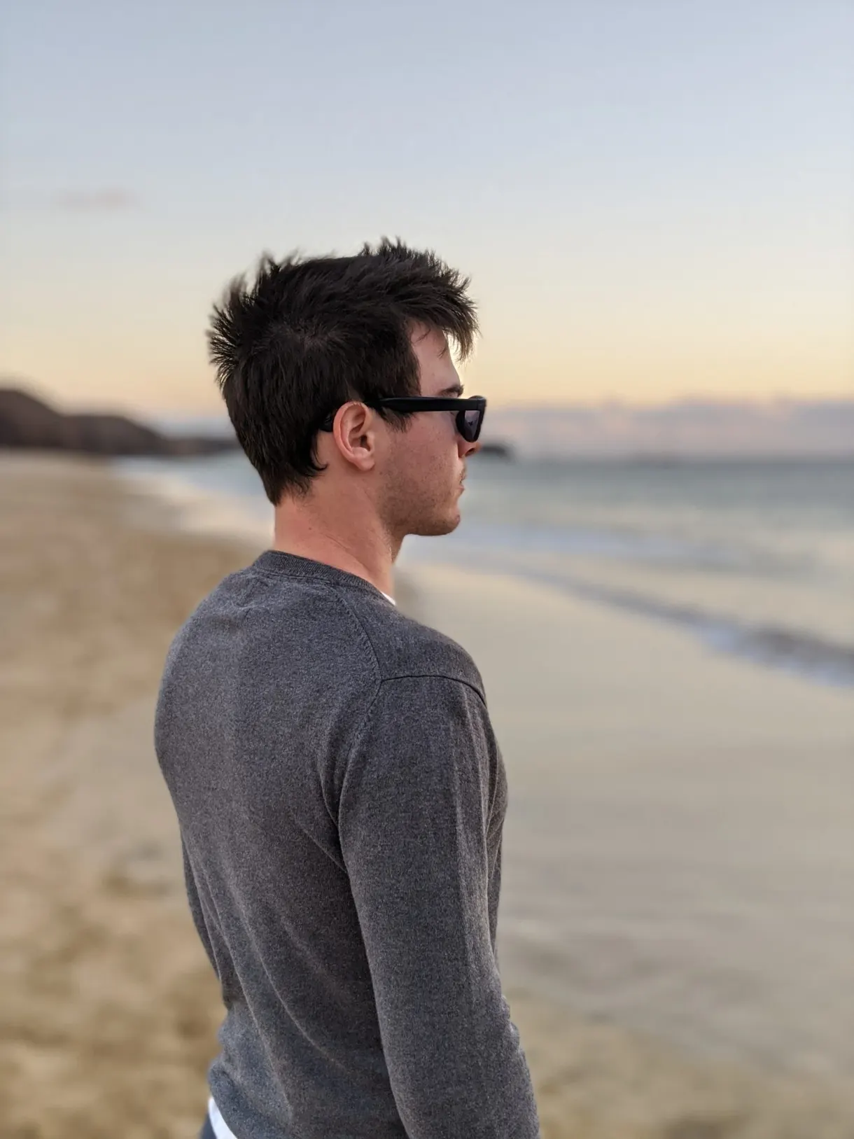 Homme de profil en pull gris sur la plage au crépuscule