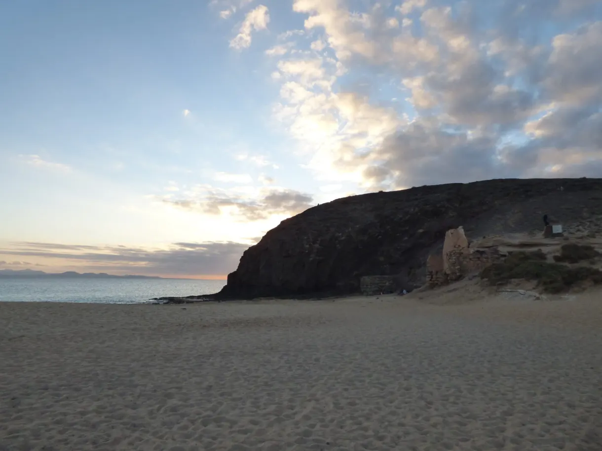 Falaise sombre et nuages roses au-dessus du sable