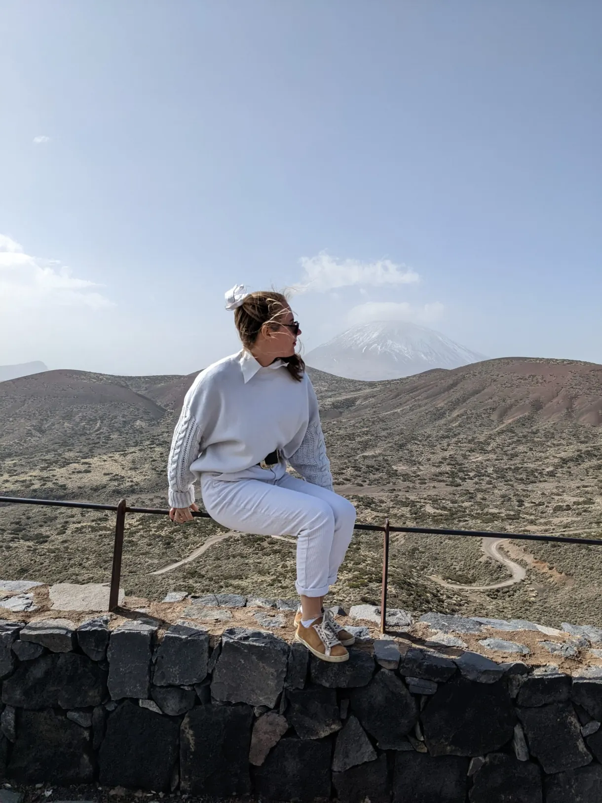 Woman sitting on a low wall facing the snow-capped summit