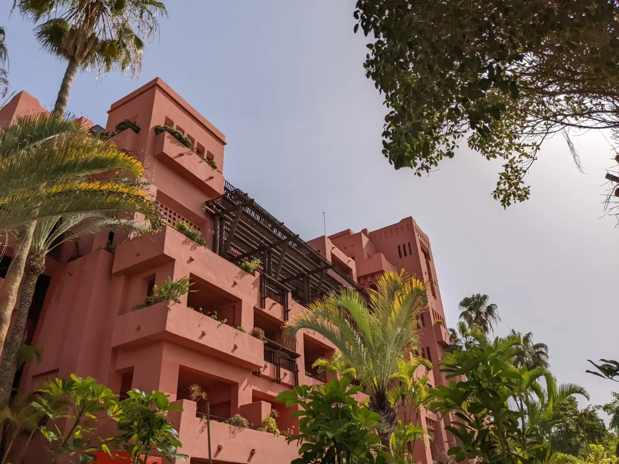 Bâtiment rose orangé de l'hôtel entouré de palmiers