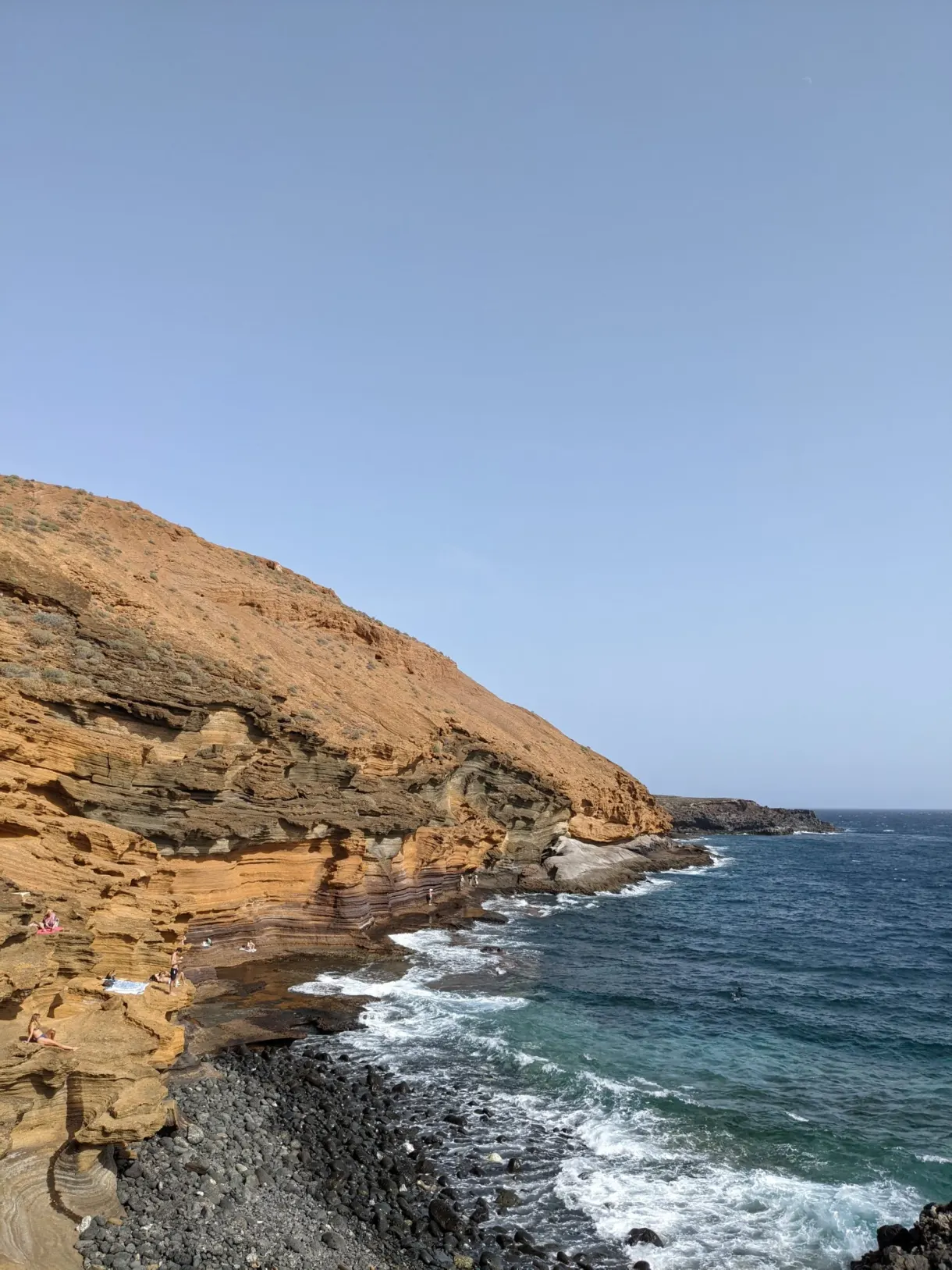 Falaise ocre dorée descendant vers une mer agitée
