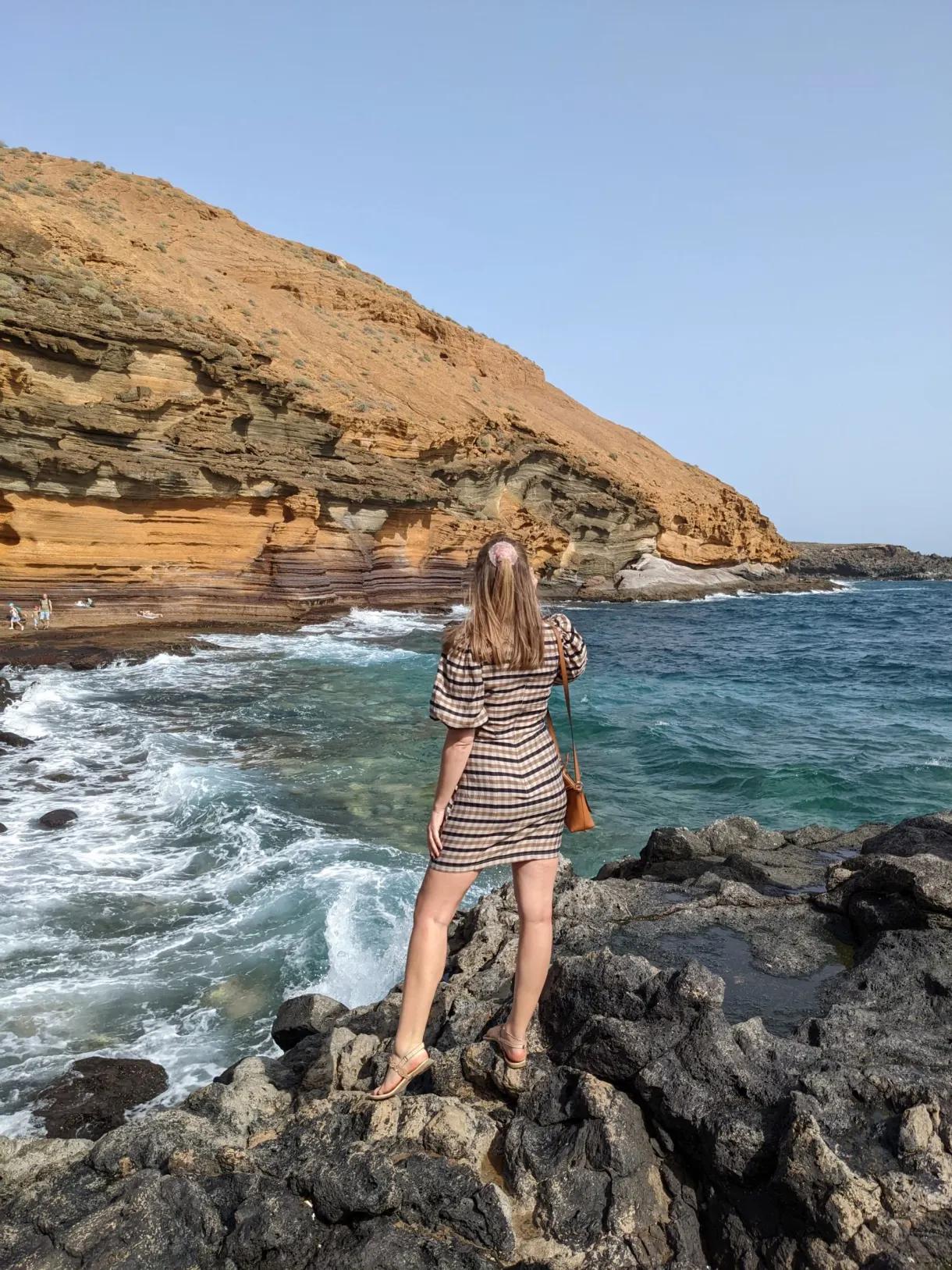 Femme de dos sur les rochers noirs face aux vagues et à la falaise