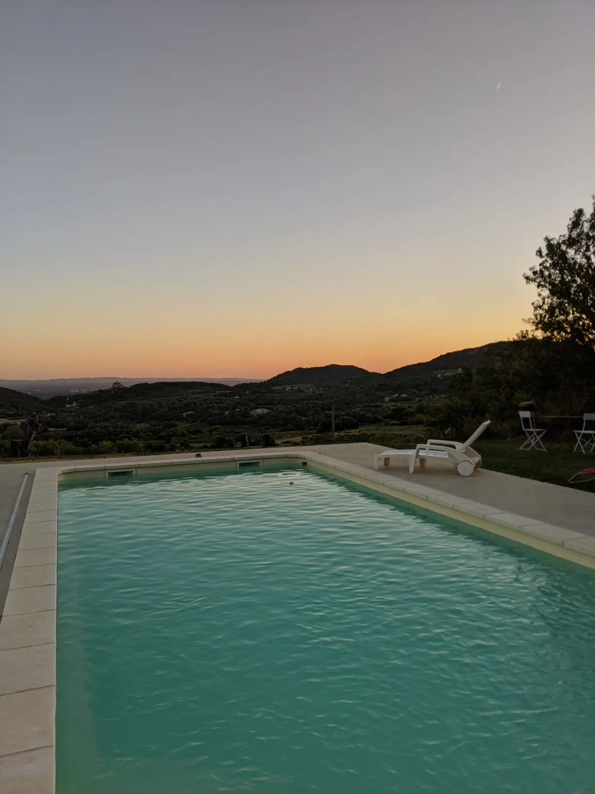 Turquoise pool and sun loungers facing the orange sky at dusk