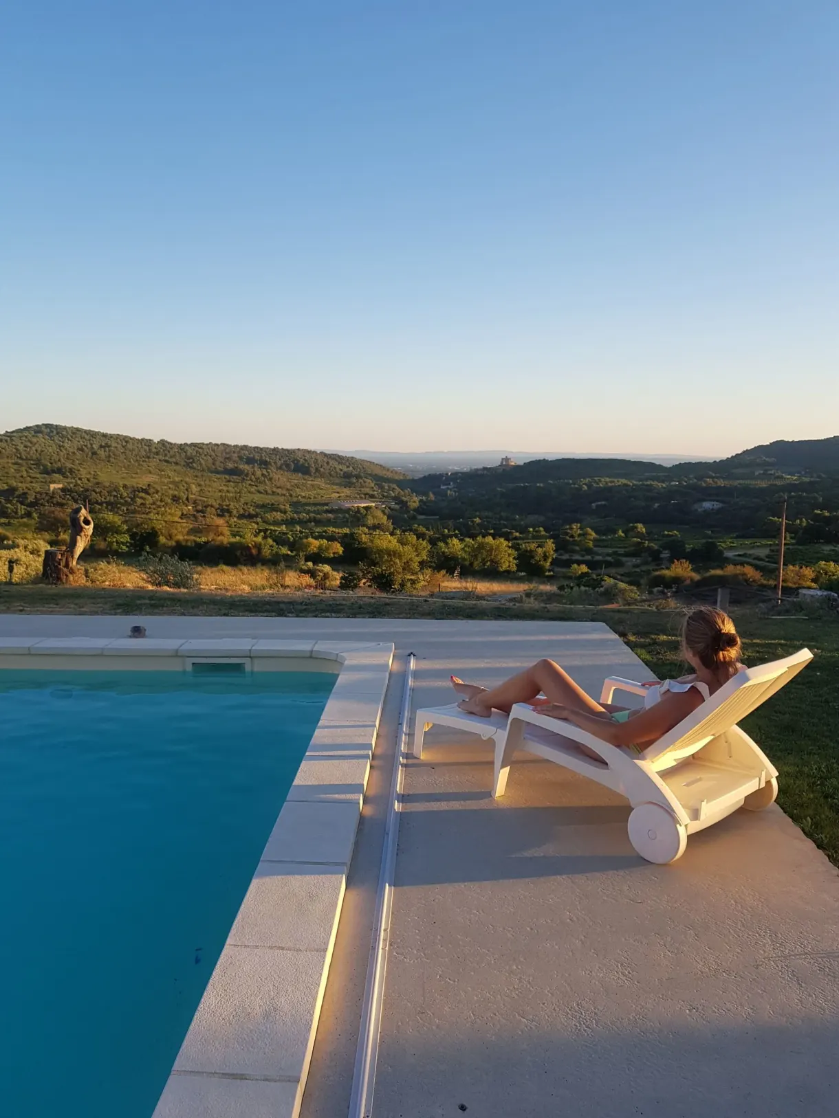 Woman lying on a sun lounger at the edge of the pool at sunset
