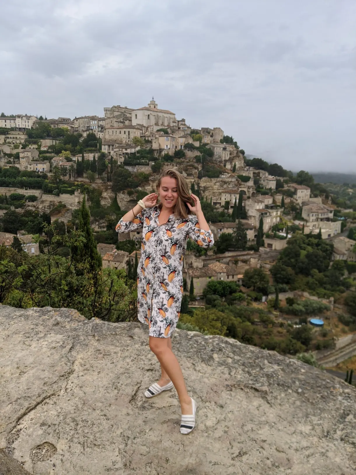 Femme posant sur un rocher devant un village perché