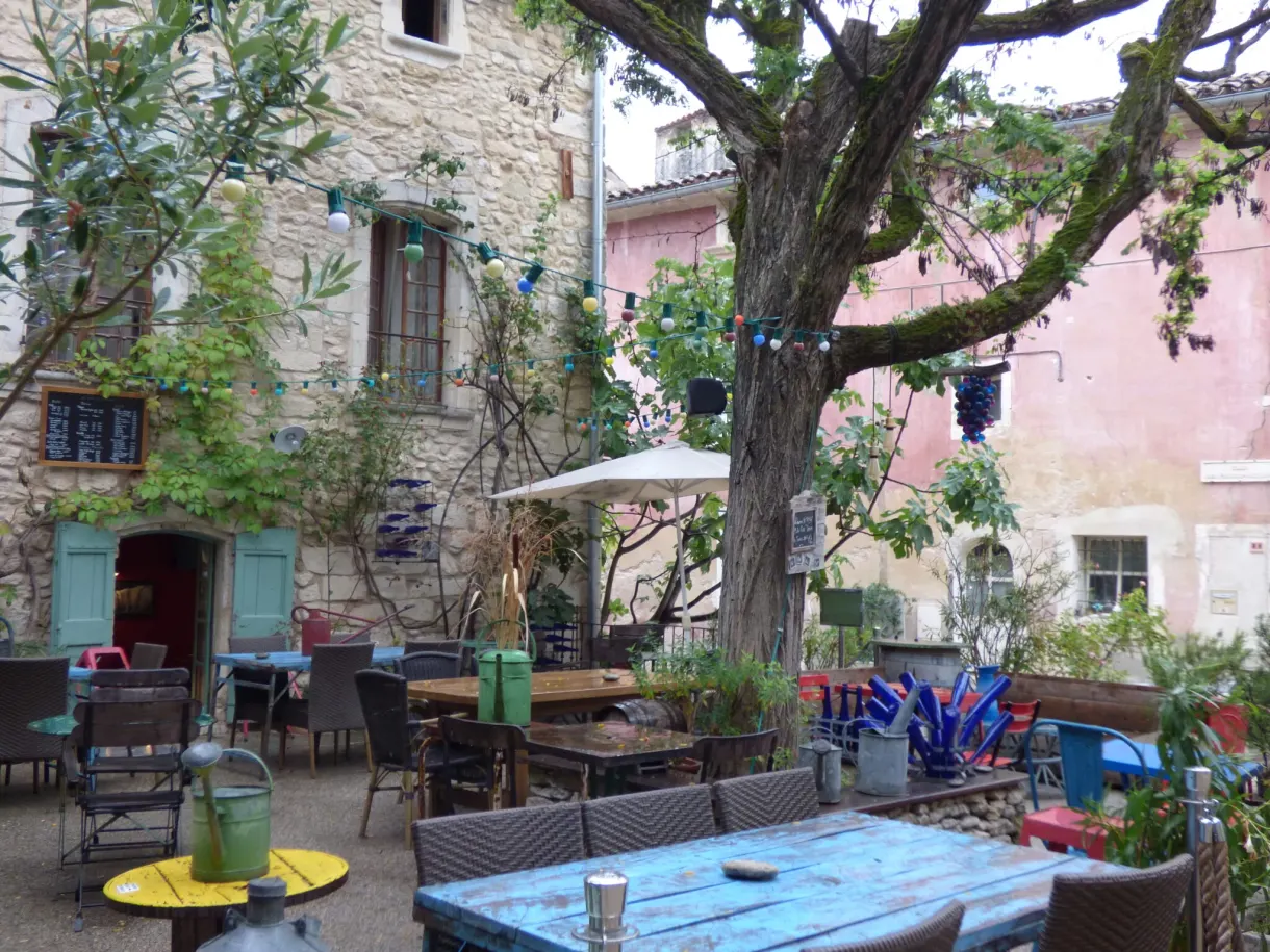Terrasse de café aux tables colorées sous les platanes