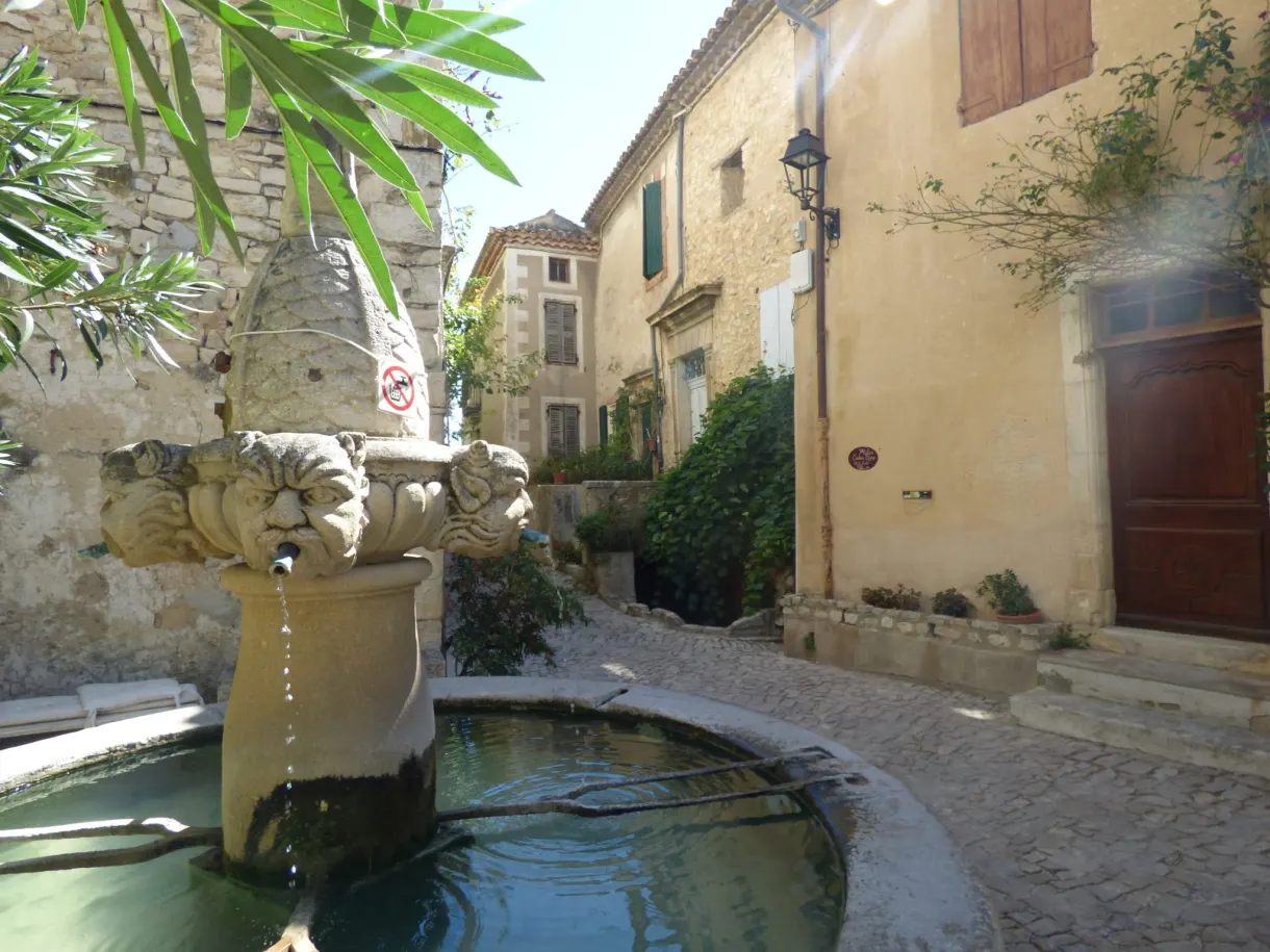 Fountain with mascarons and its round basin in a cobbled lane