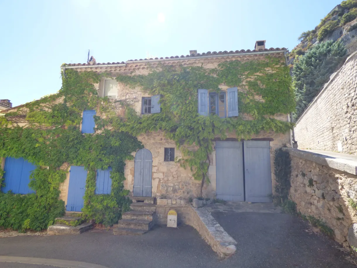 Stone house overrun with Virginia creeper beneath the cliff
