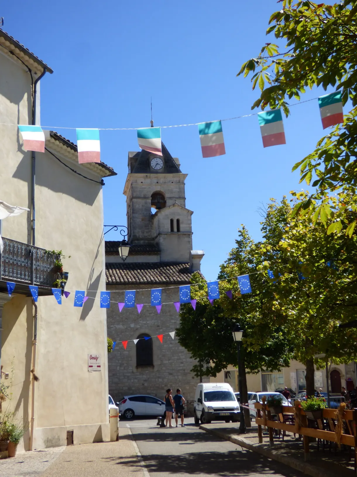 Colourful bunting stretched in front of the bell tower of a lively village