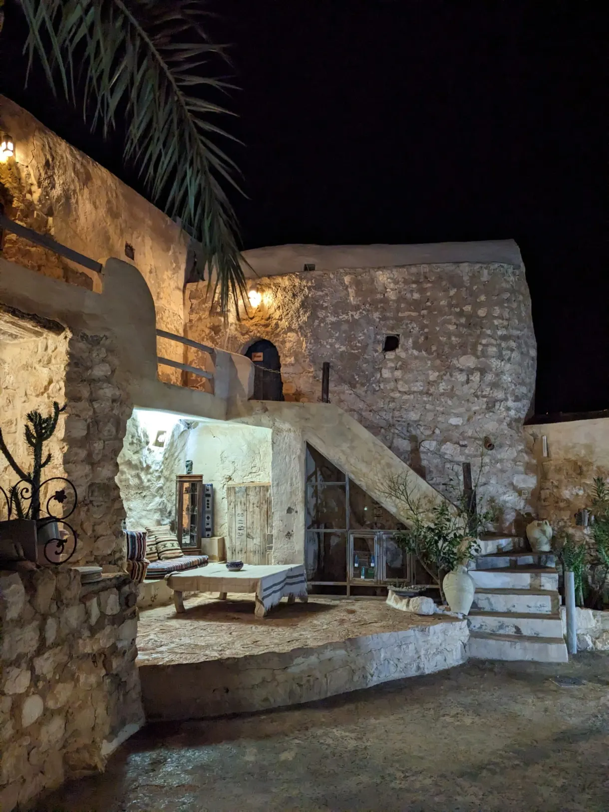 Cour de l'Auberge de Tamezret la nuit, murs de pierre éclairés et escalier vers les chambres