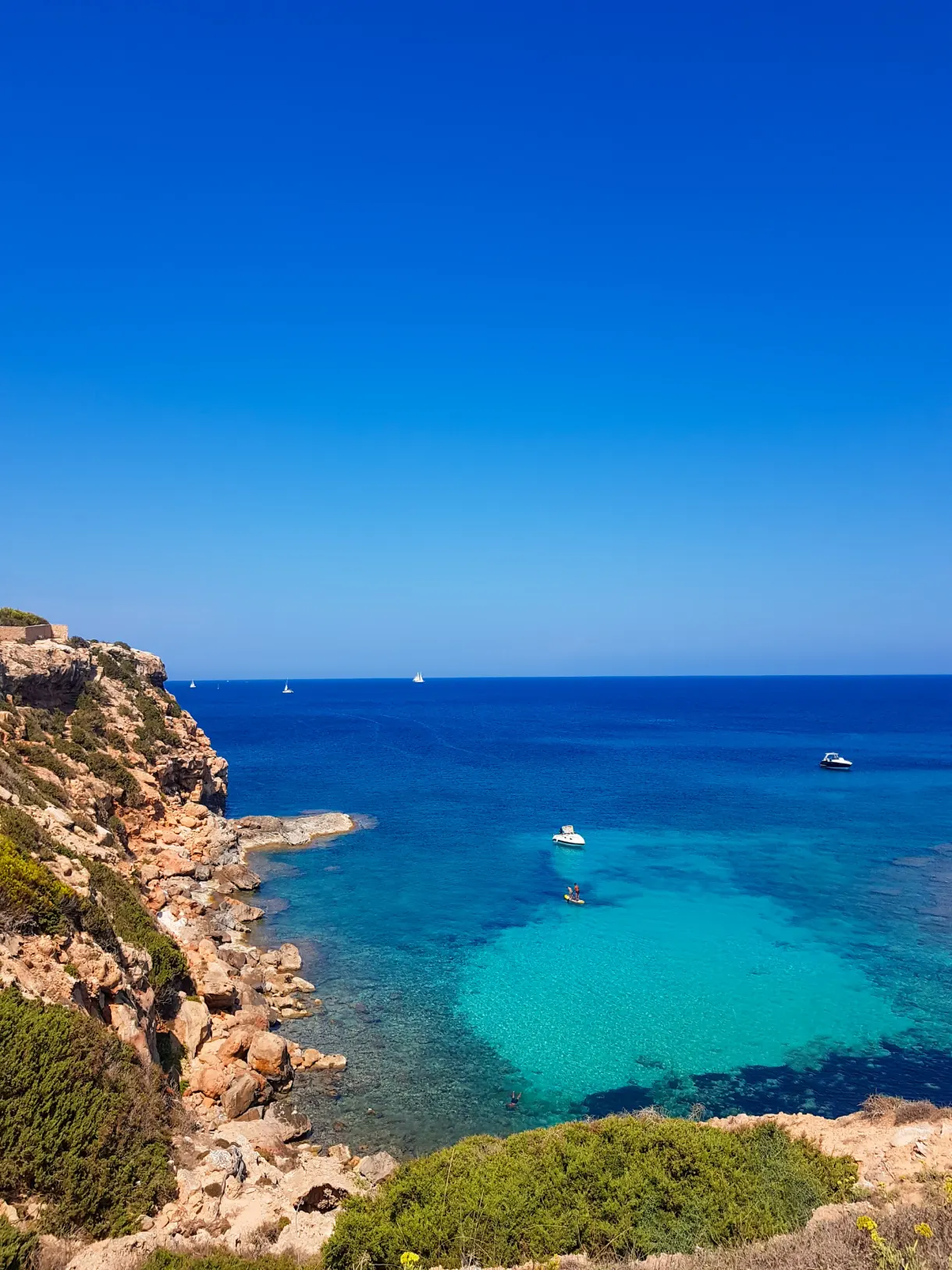 Turquoise cove lined with rocks and sailing boats