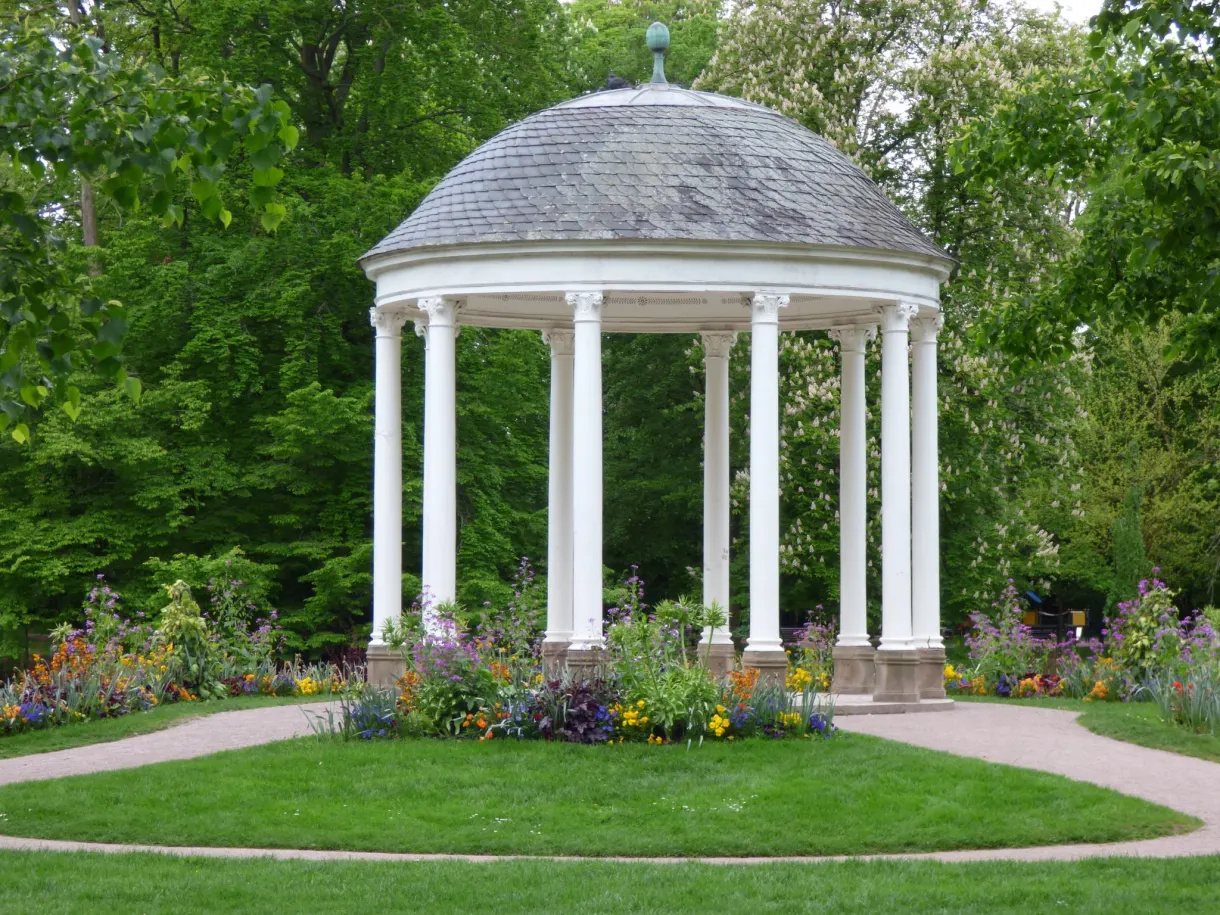 Small temple with white columns surrounded by flower beds