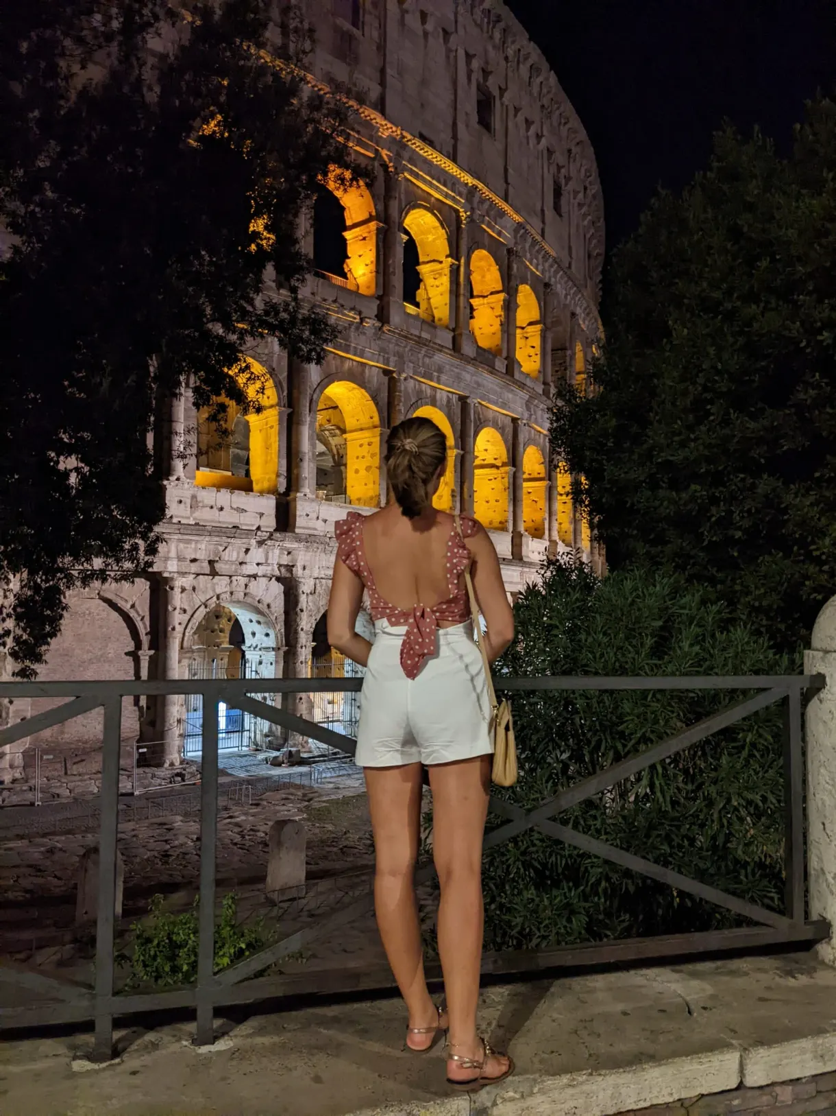 Femme de dos devant l'amphithéâtre éclairé le soir