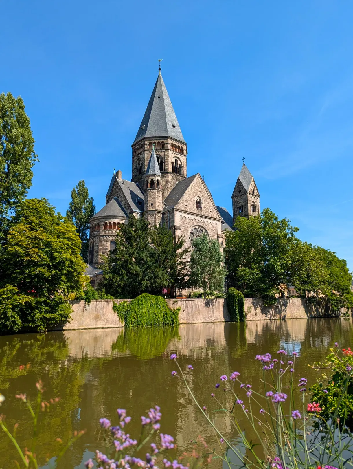 Clocher de pierre grise au bord de l'eau à Metz, fleurs roses au premier plan