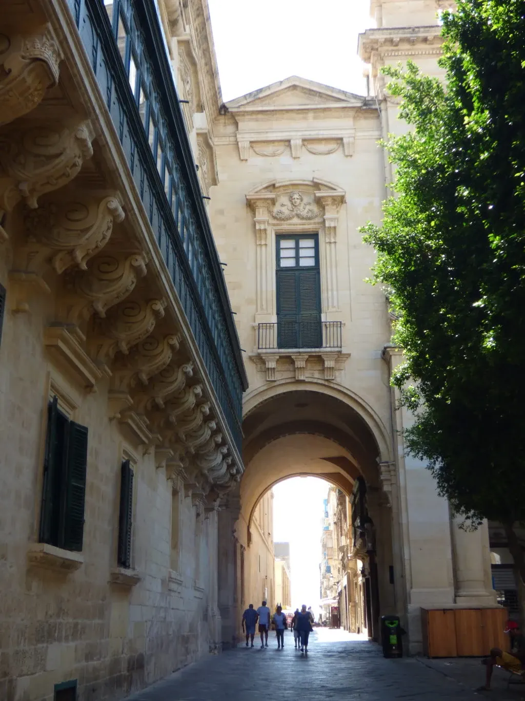 Lane passing under an arch, ornate balconies and a green tree