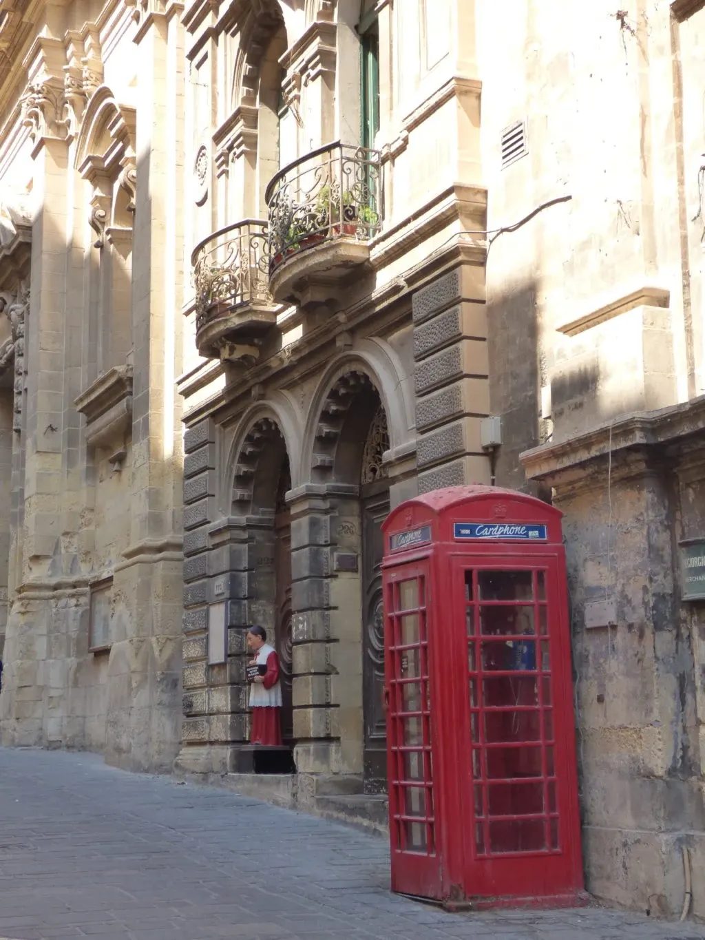Red telephone box at the foot of a facade with stone balconies