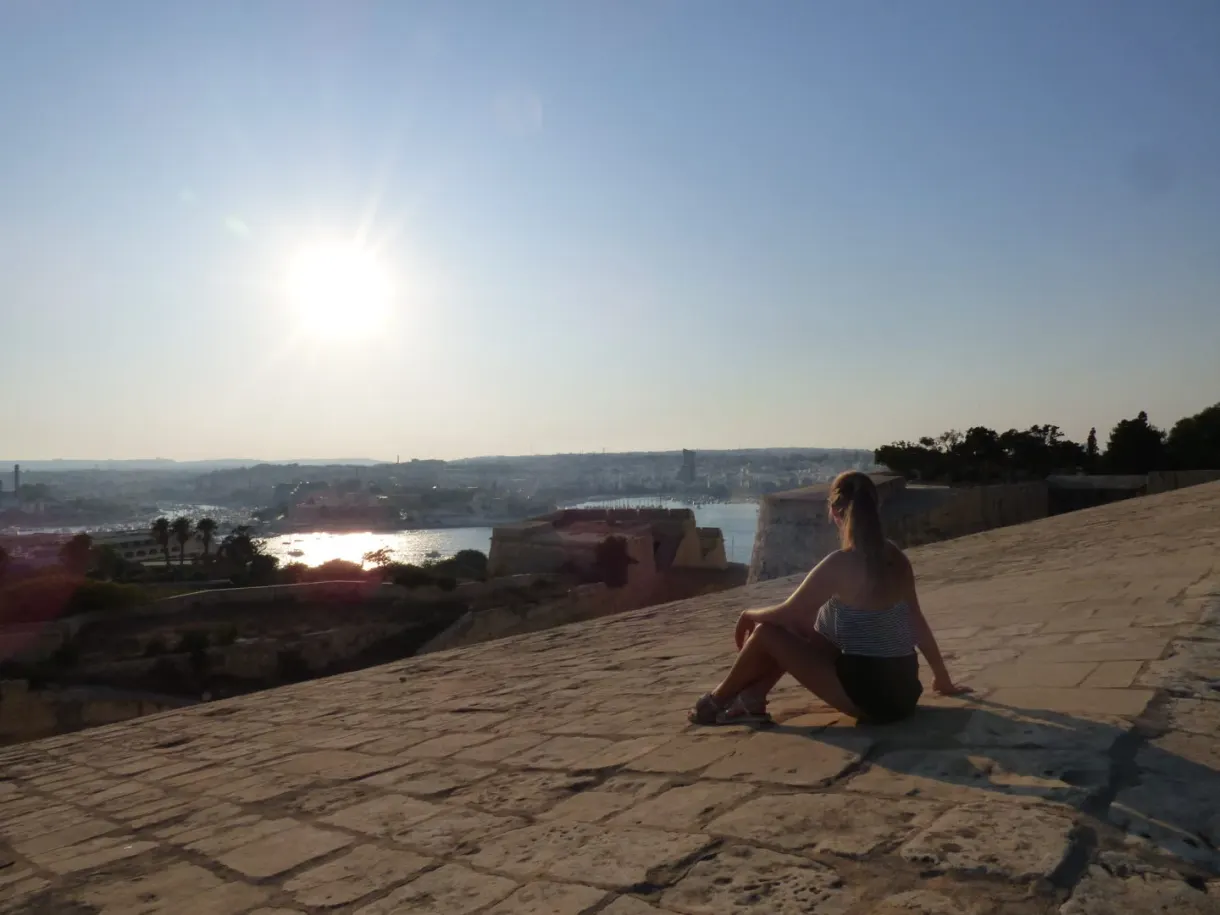 Woman sitting on the rampart facing the setting sun
