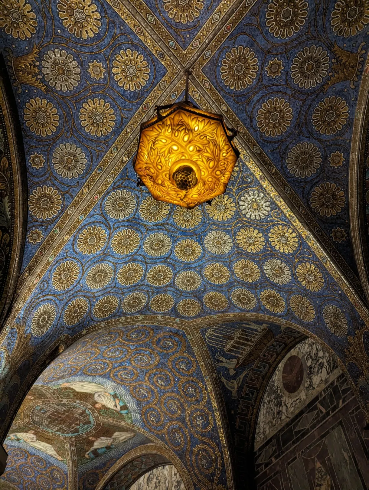 Gilded chandelier hanging beneath a blue vault dotted with mosaics