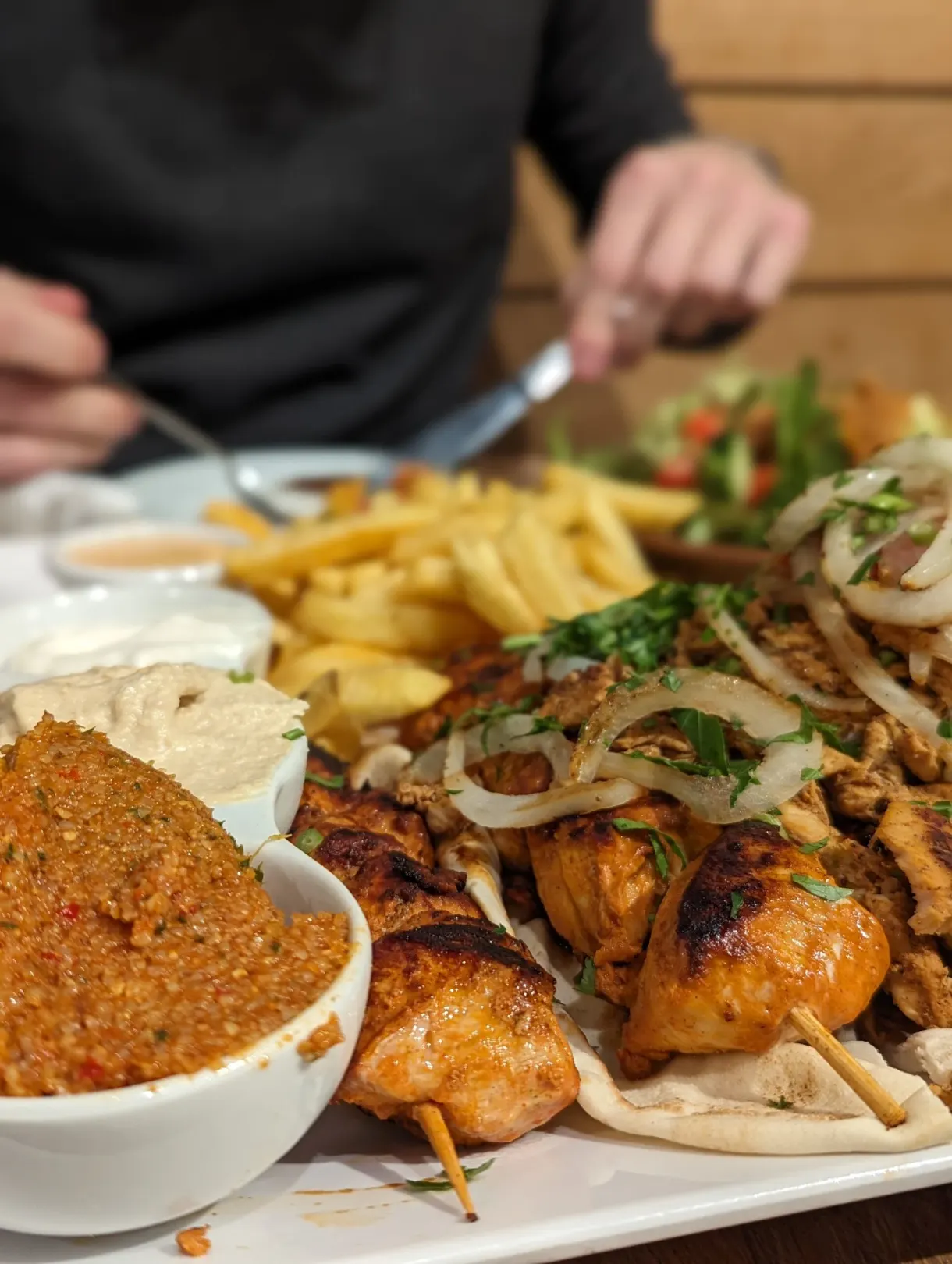 Grilled skewers, fries and hummus shared at the table