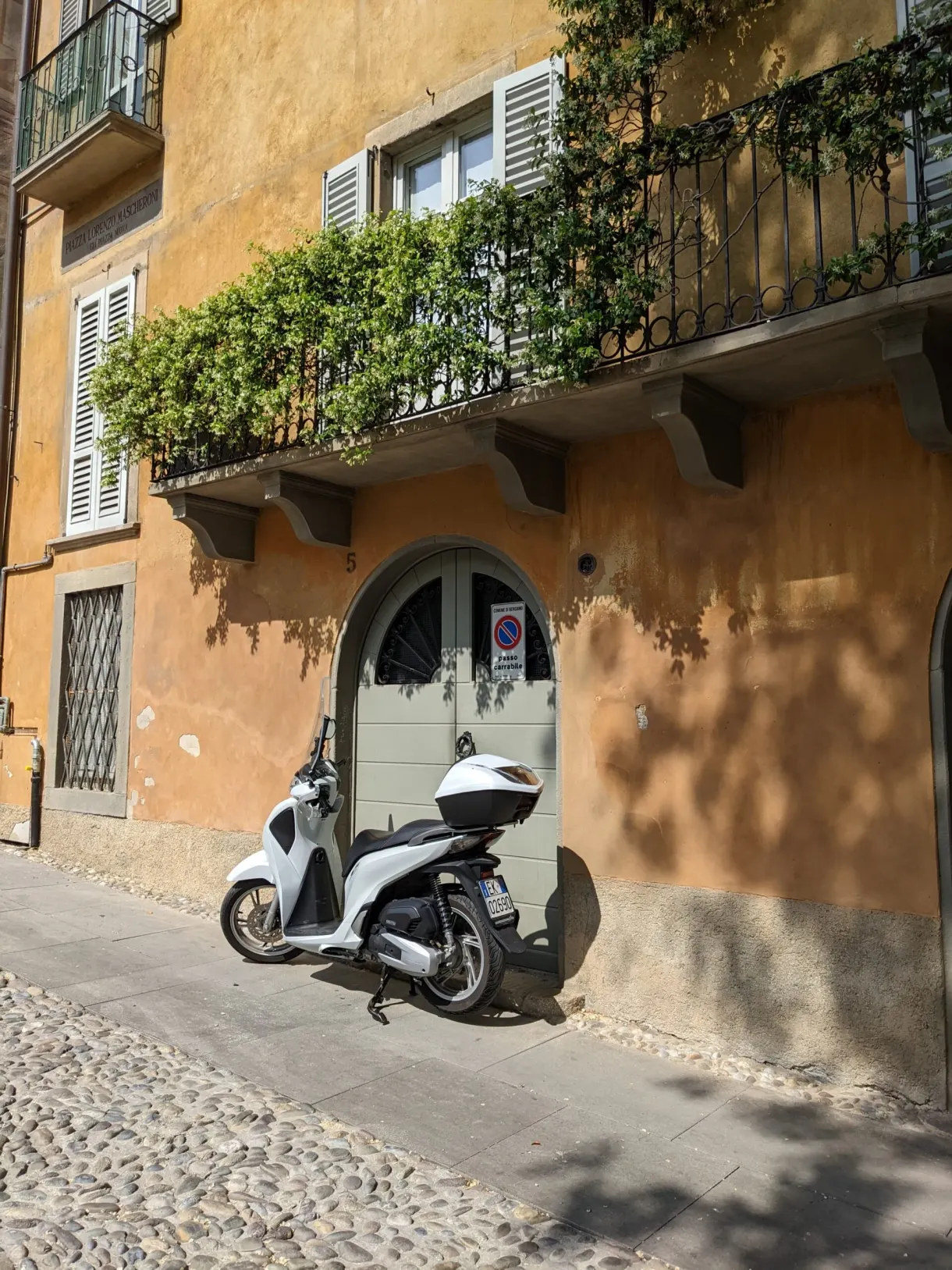 White scooter parked beneath a flower-decked balcony on an ochre facade