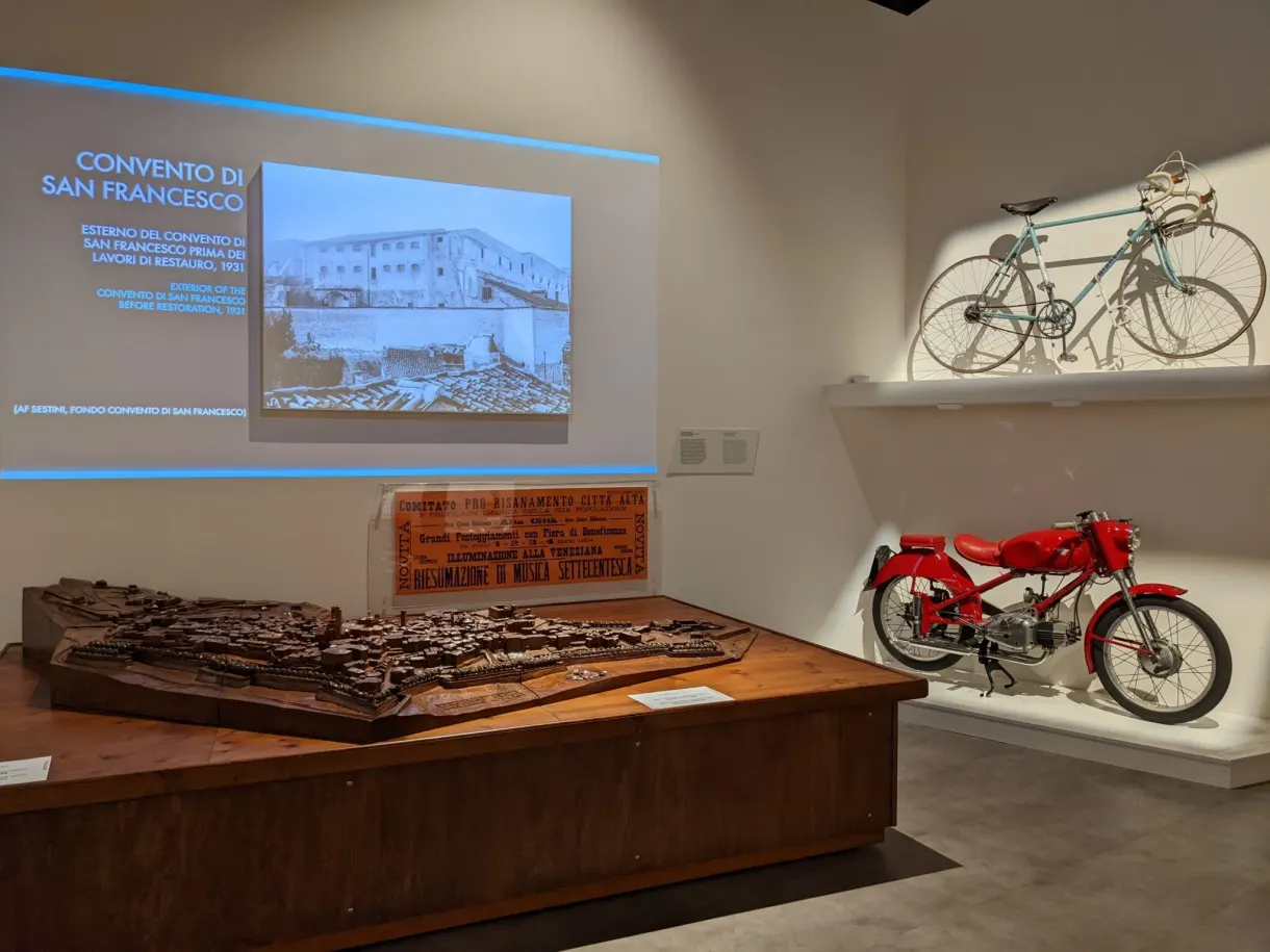 Exhibition room with a wooden model and a red moped