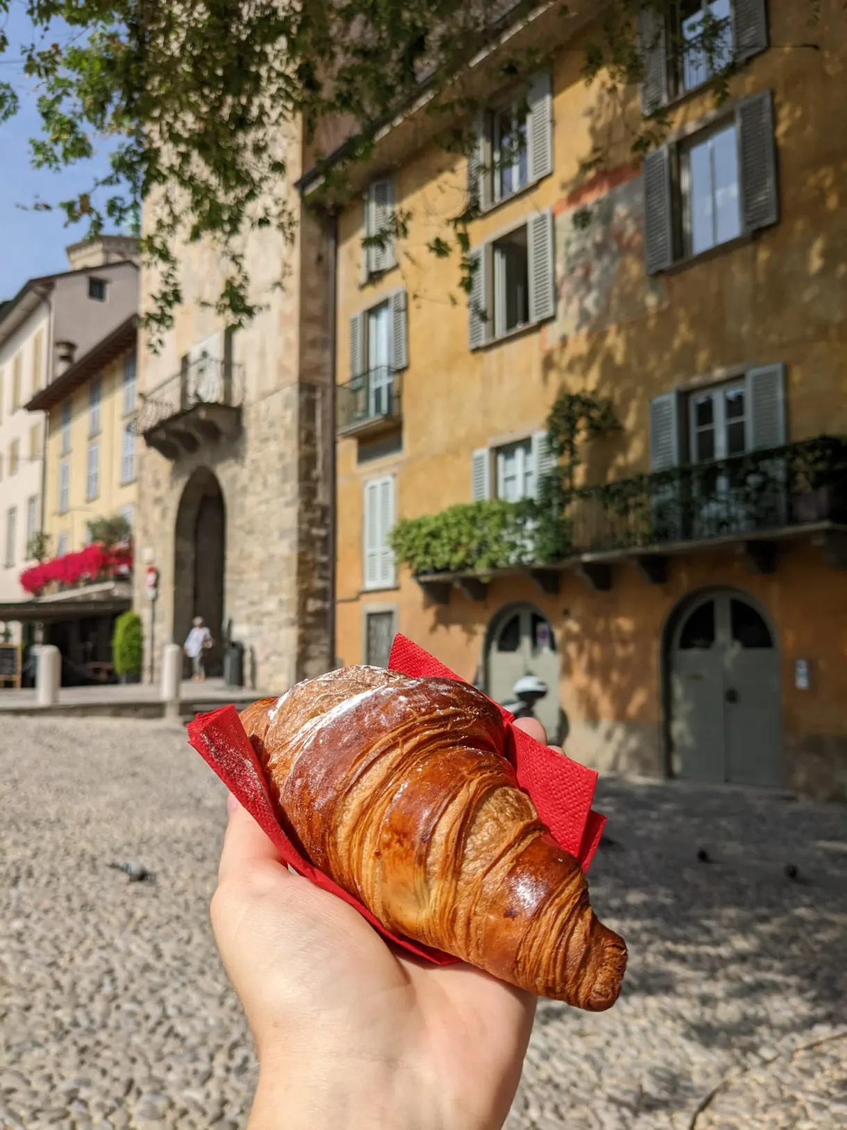 Croissant held in the hand in front of an ochre facade
