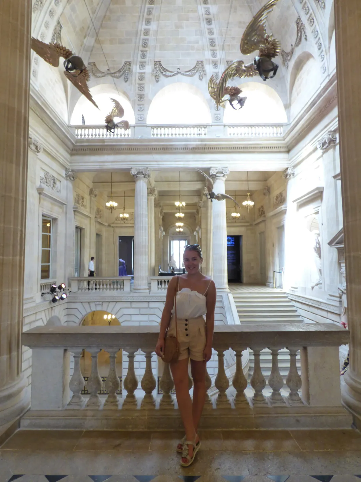 Femme au bas d'un escalier monumental sous une voûte à colonnes