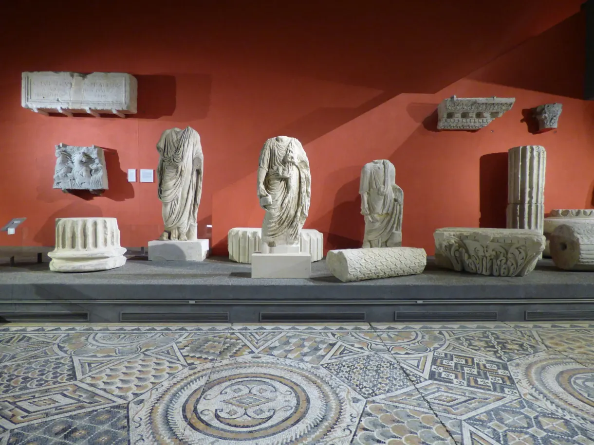 Statues antiques et mosaïque au sol devant un mur rouge de musée