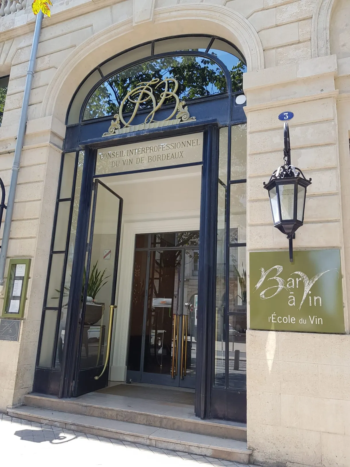 Porte vitrée cintrée d'un bar à vin sous une lanterne de fer