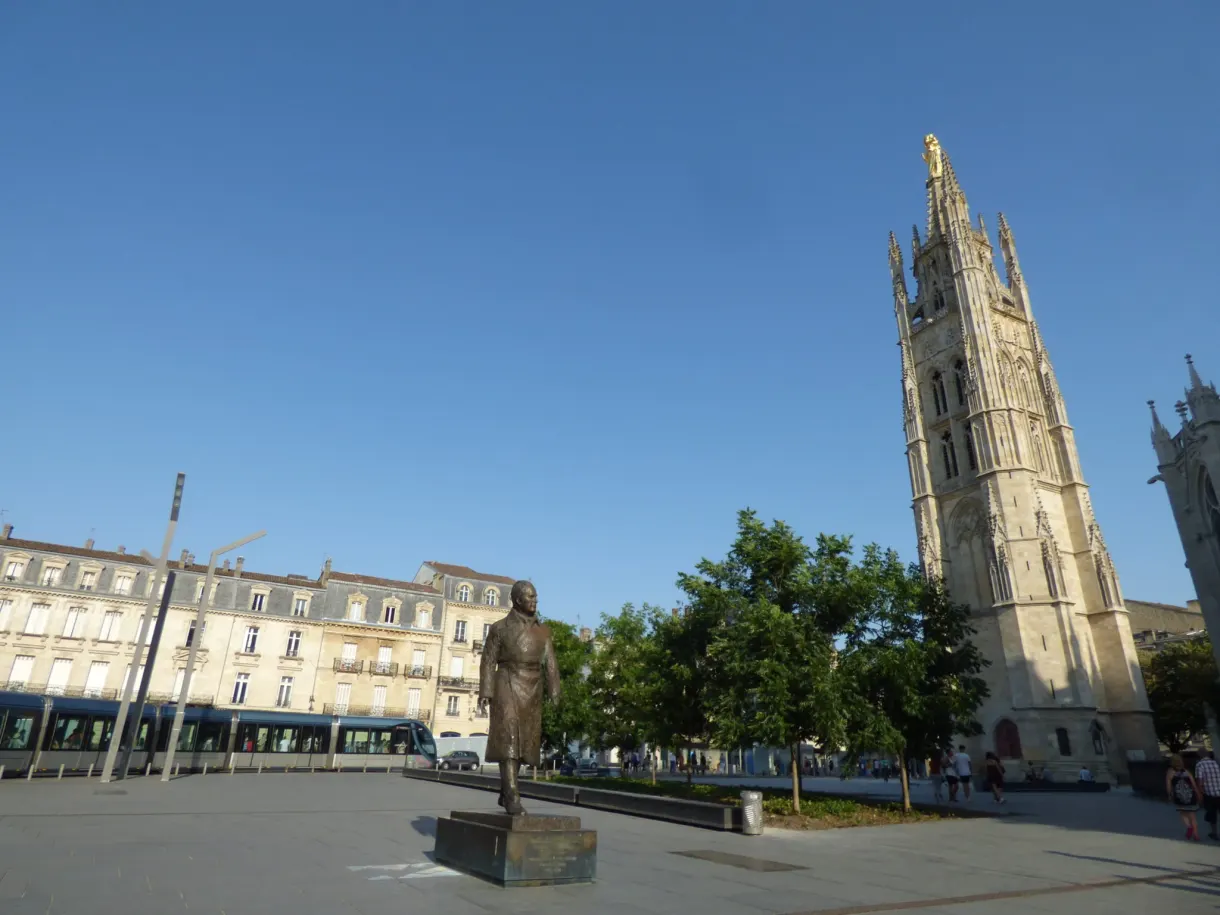Esplanade dallée avec une statue sombre et la flèche de la cathédrale