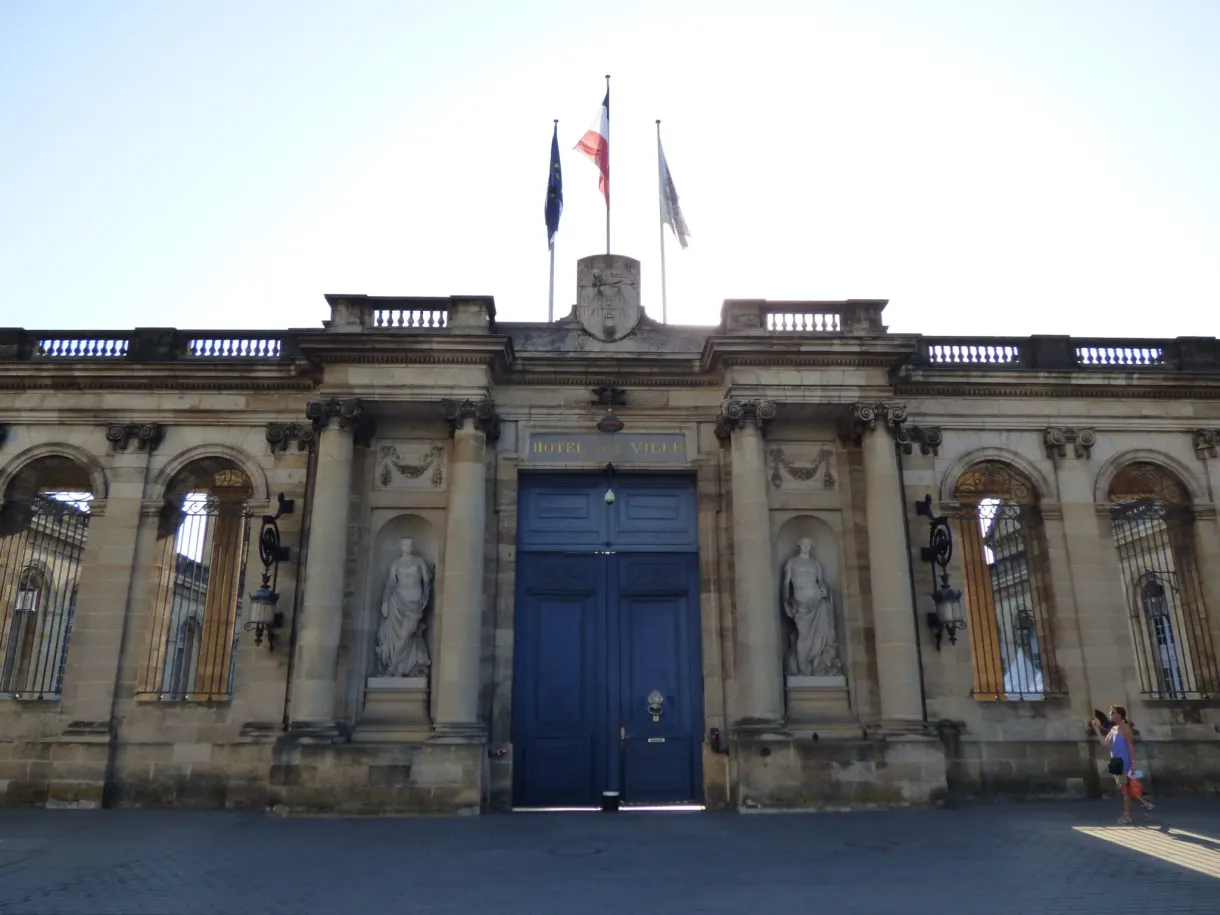 Façade à colonnes et porte bleue surmontée de drapeaux tricolores
