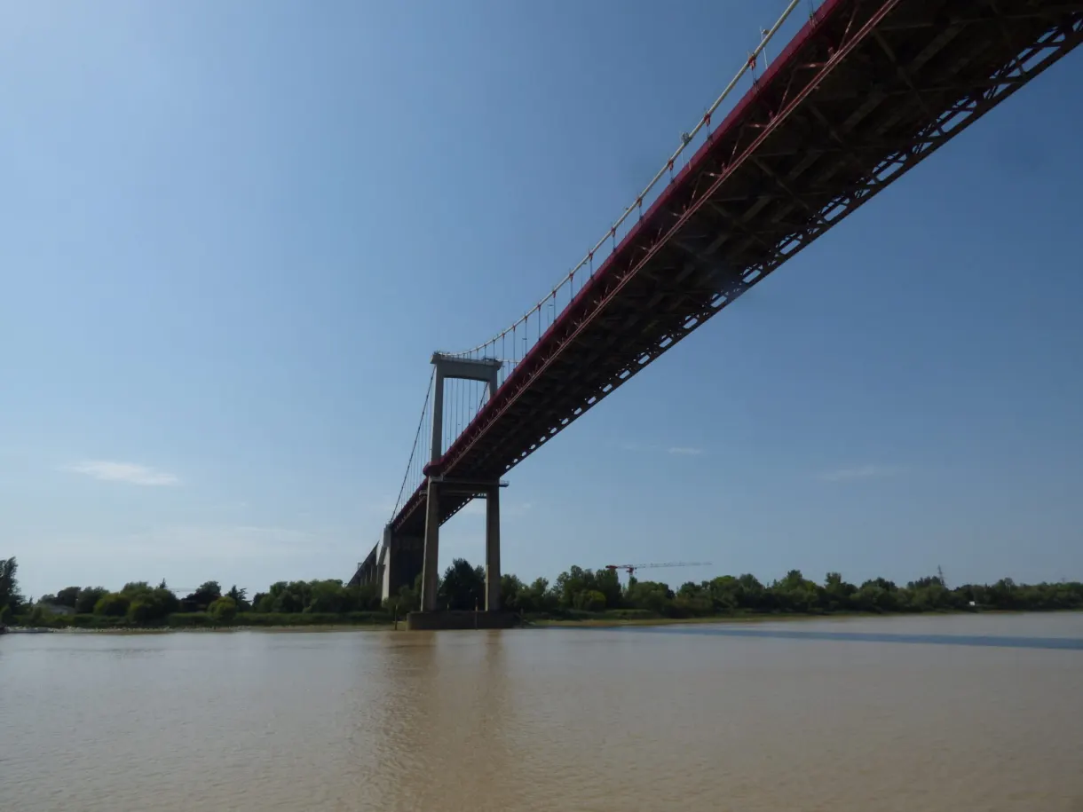 Dessous du tablier rouge d'un pont suspendu au ras de la Garonne
