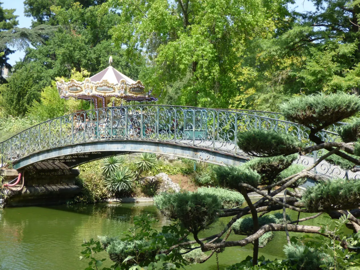Manège coloré aperçu derrière une passerelle et un pin taillé