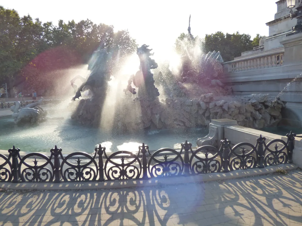Gerbes d'eau de la fontaine éclatant à contre-jour derrière une grille