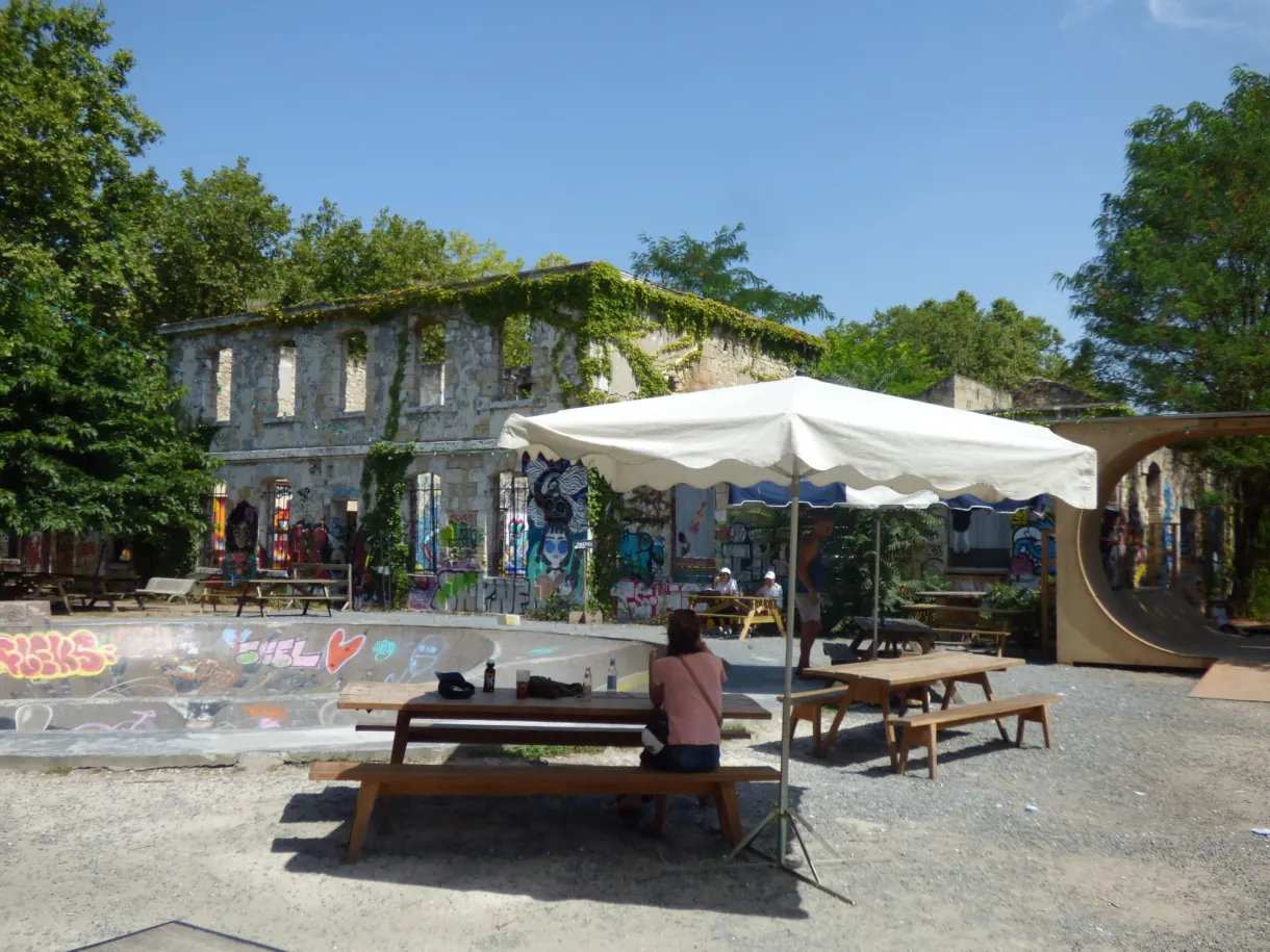 Parasol blanc et bancs de bois devant des murs couverts de graffitis