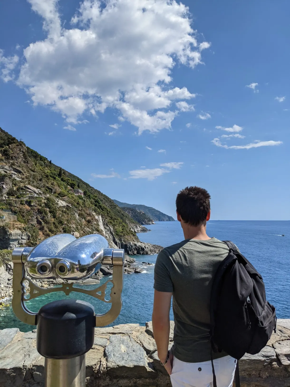 Voyageur de dos près d'une longue-vue face à la mer