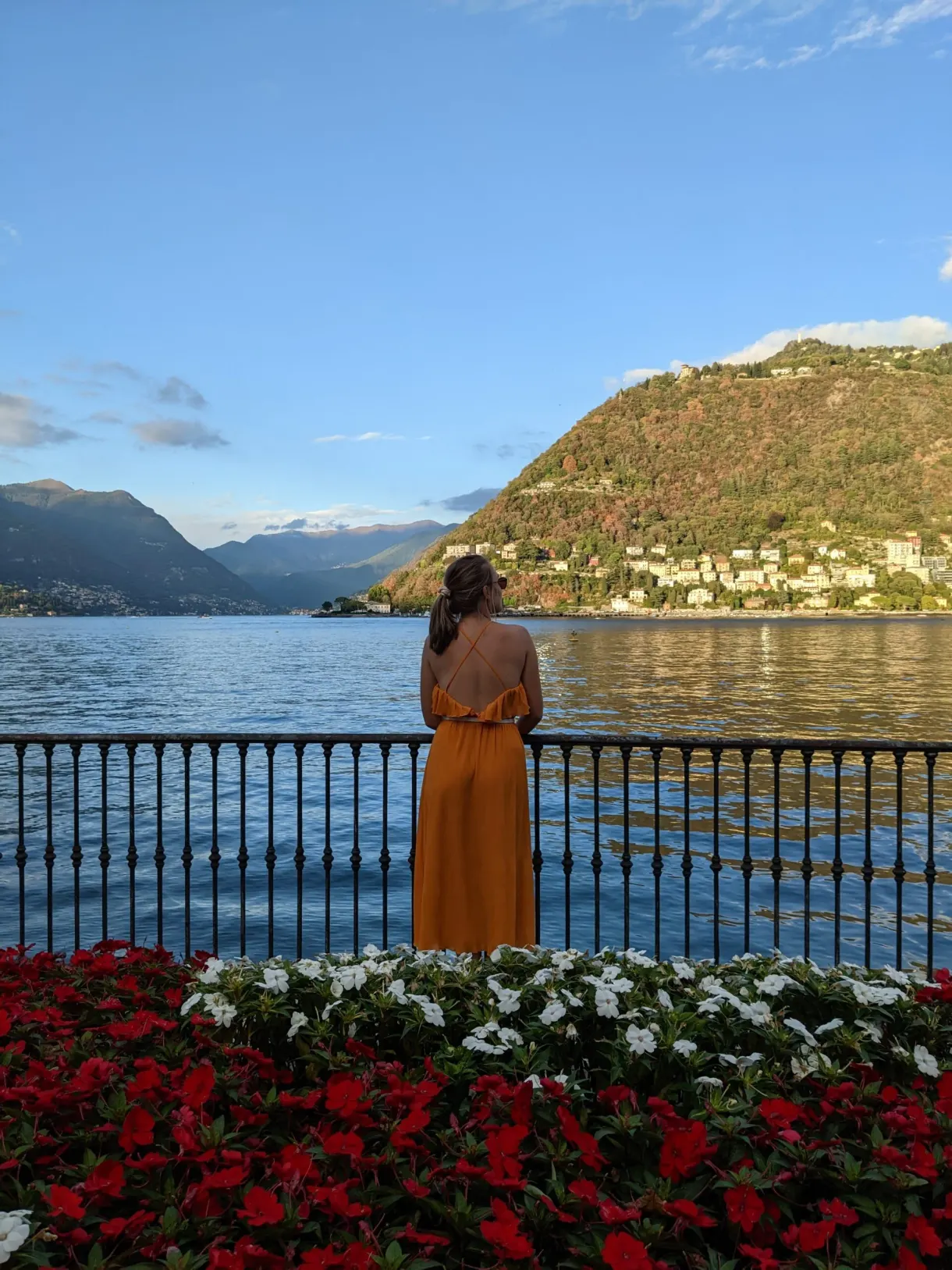 Femme en robe orange accoudée au garde-corps fleuri de rouge