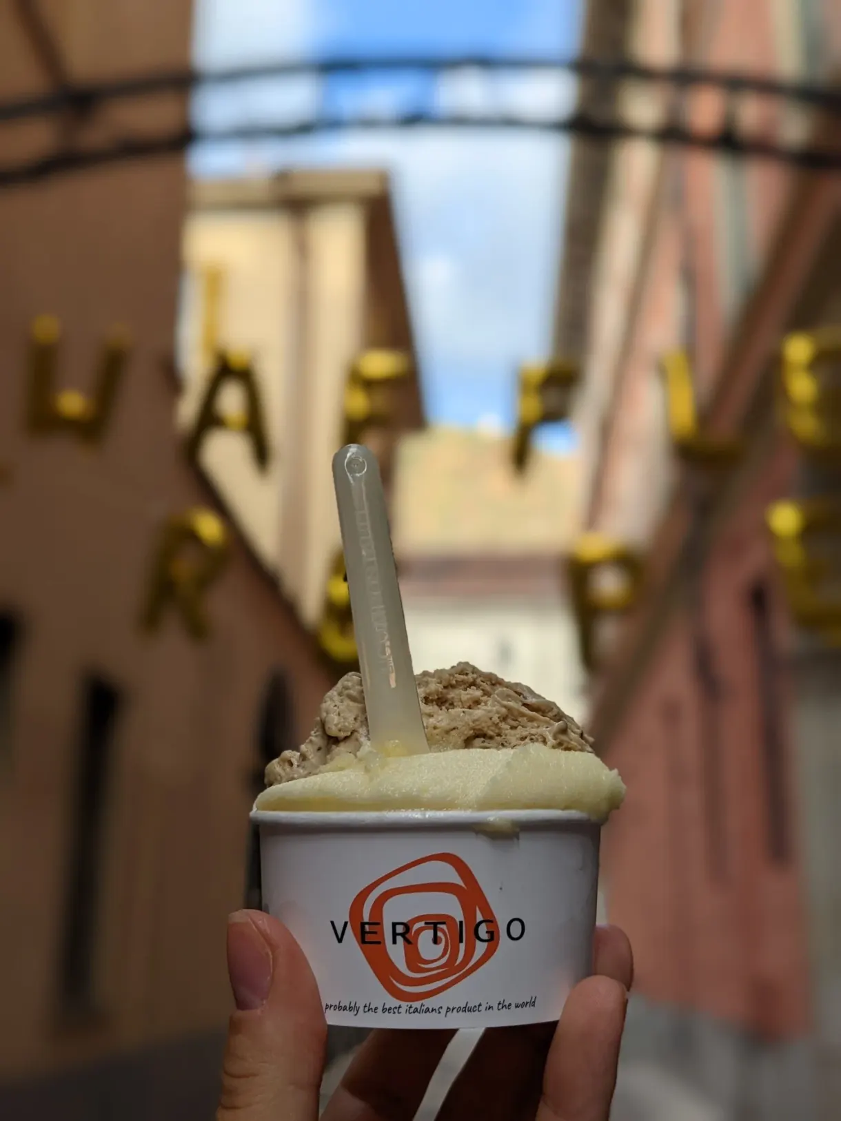 Pot de glace tenu devant les façades colorées d'une ruelle