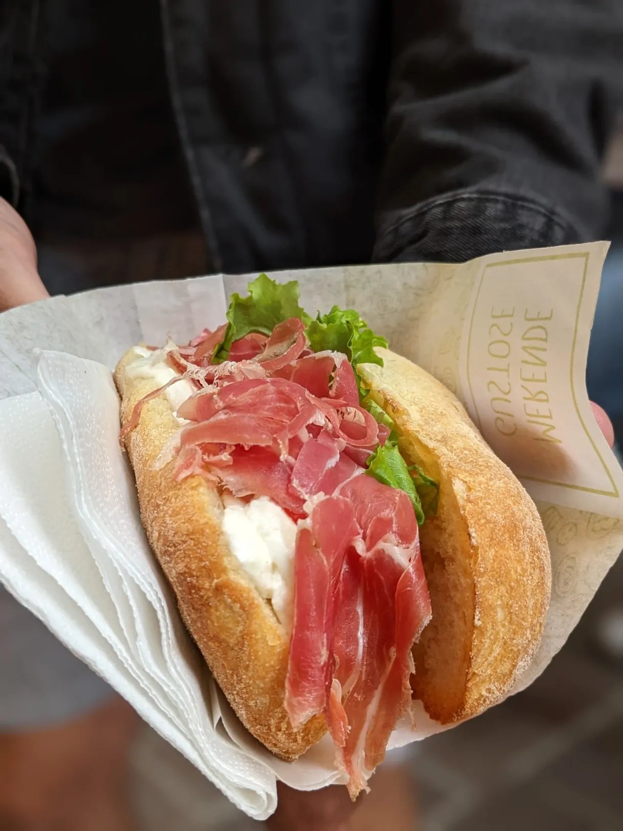 Sandwich au jambon cru tenu à la main dans son papier