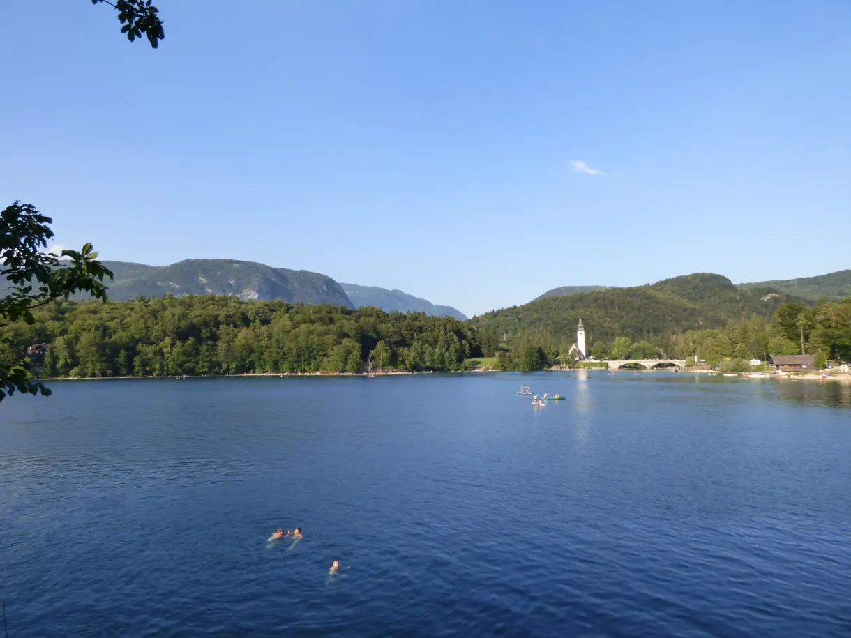 Baigneurs dans l'eau calme face au clocher lointain