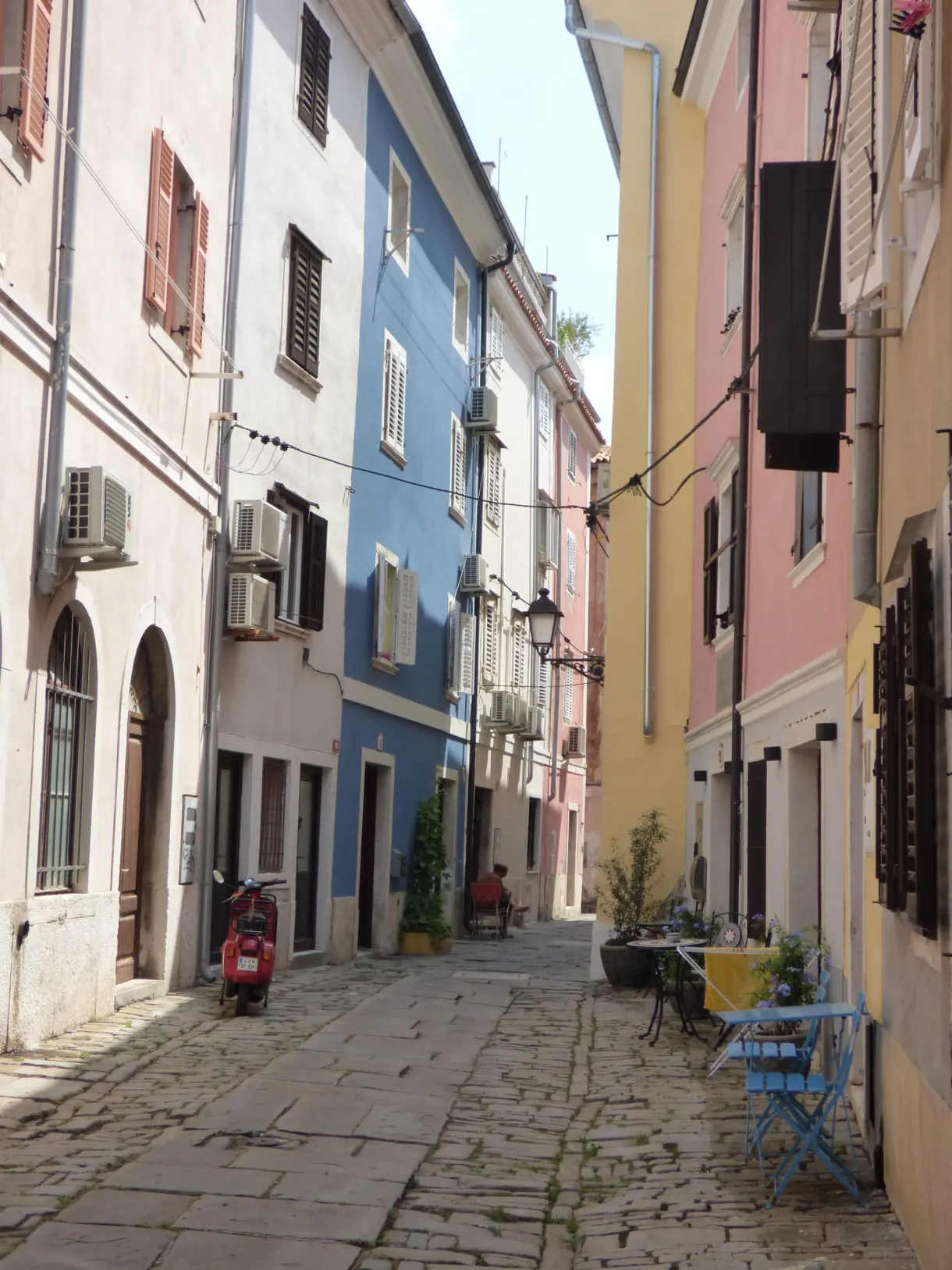 Cobbled lane with blue and yellow facades, bistro chairs