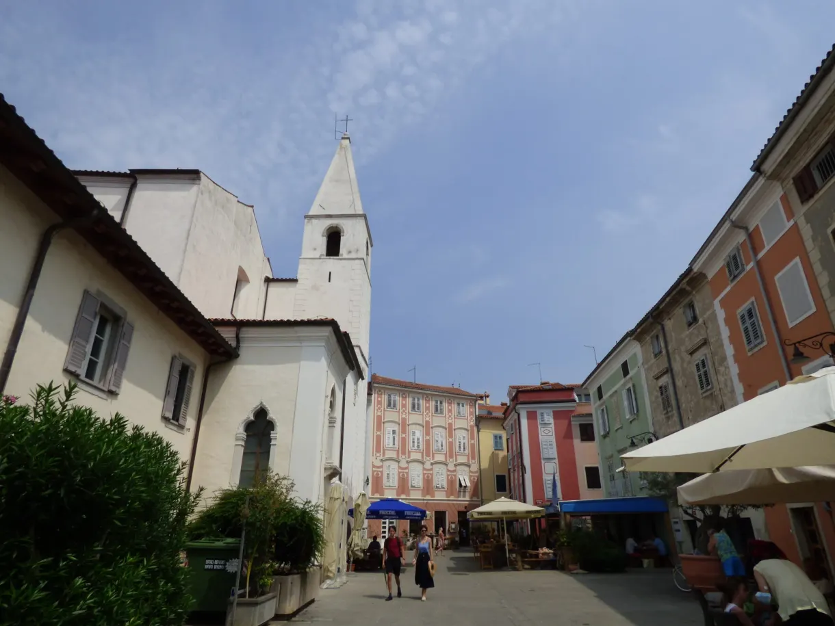 White church and cafe terraces on a square in Izola