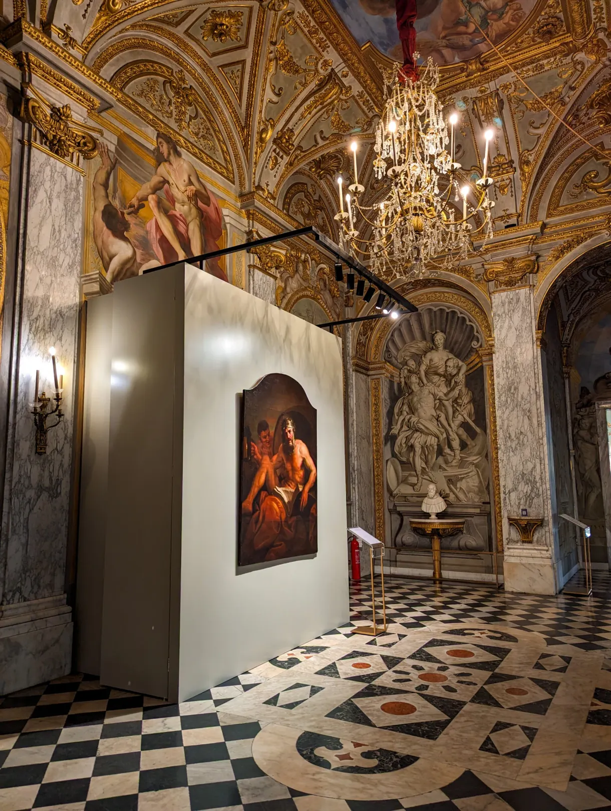 Old painting hung on a display panel in a room with a chandelier