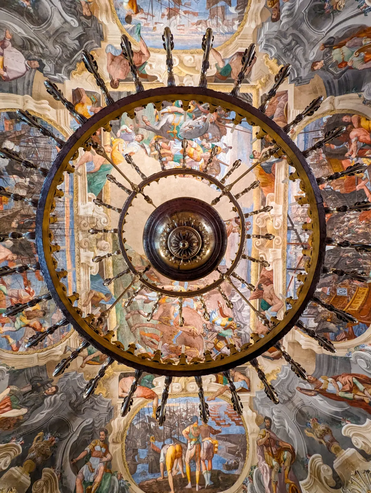 Gilded chandelier seen from below against a painted ceiling